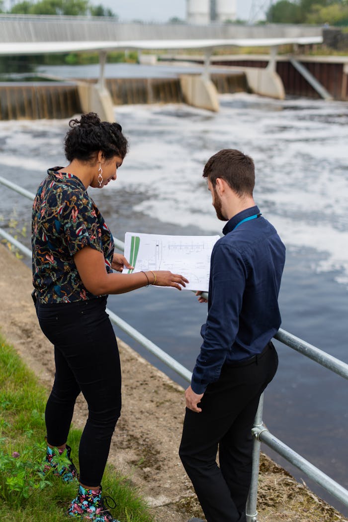 portfolio-02 Male and female engineers reviewing plans outdoors by a river dam.
