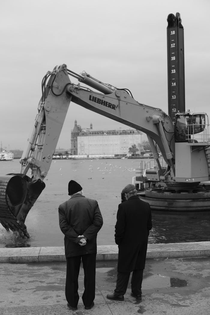 stats-img Two men observe a Liebherr excavator operating by the water, suggesting marine construction.
